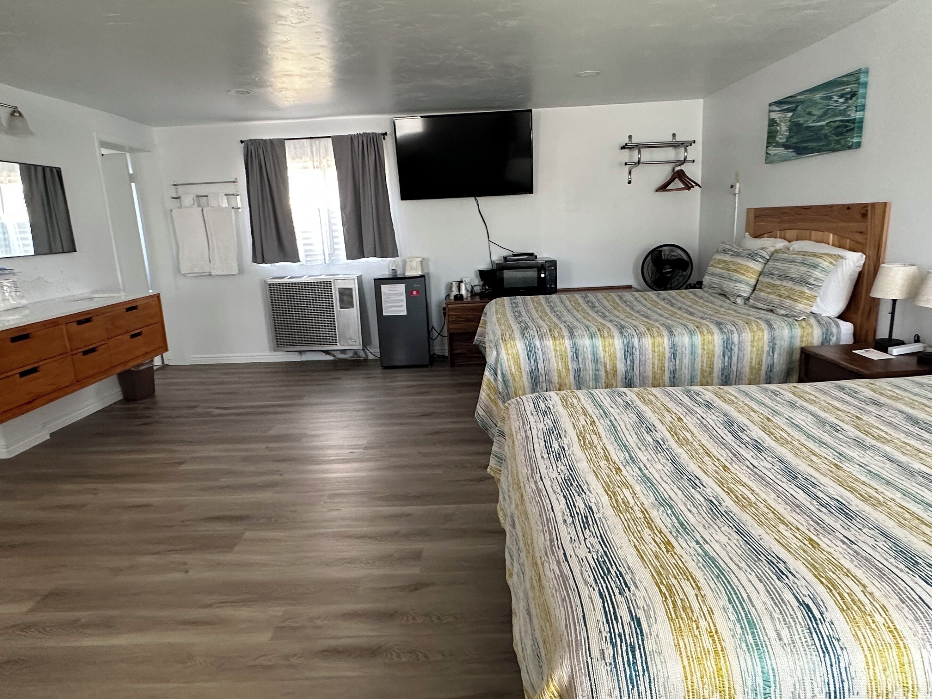 Habitación de hotel con dos camas, un aparador de madera, un televisor de pantalla plana, un equipo de aire acondicionado y un cuadro en la pared.