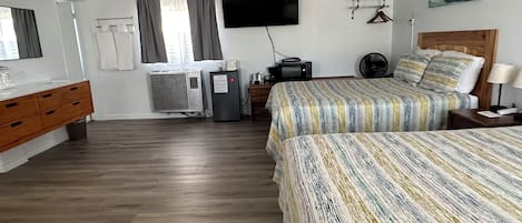 Habitación de hotel con dos camas, un aparador de madera, un televisor de pantalla plana, un equipo de aire acondicionado y un cuadro en la pared.