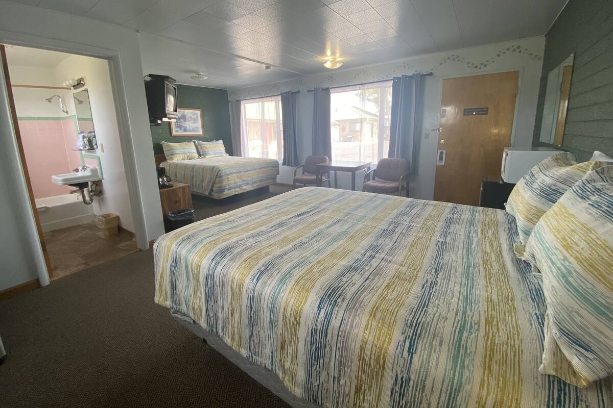 A hotel room with two beds, a bathroom, a small table, and a window.