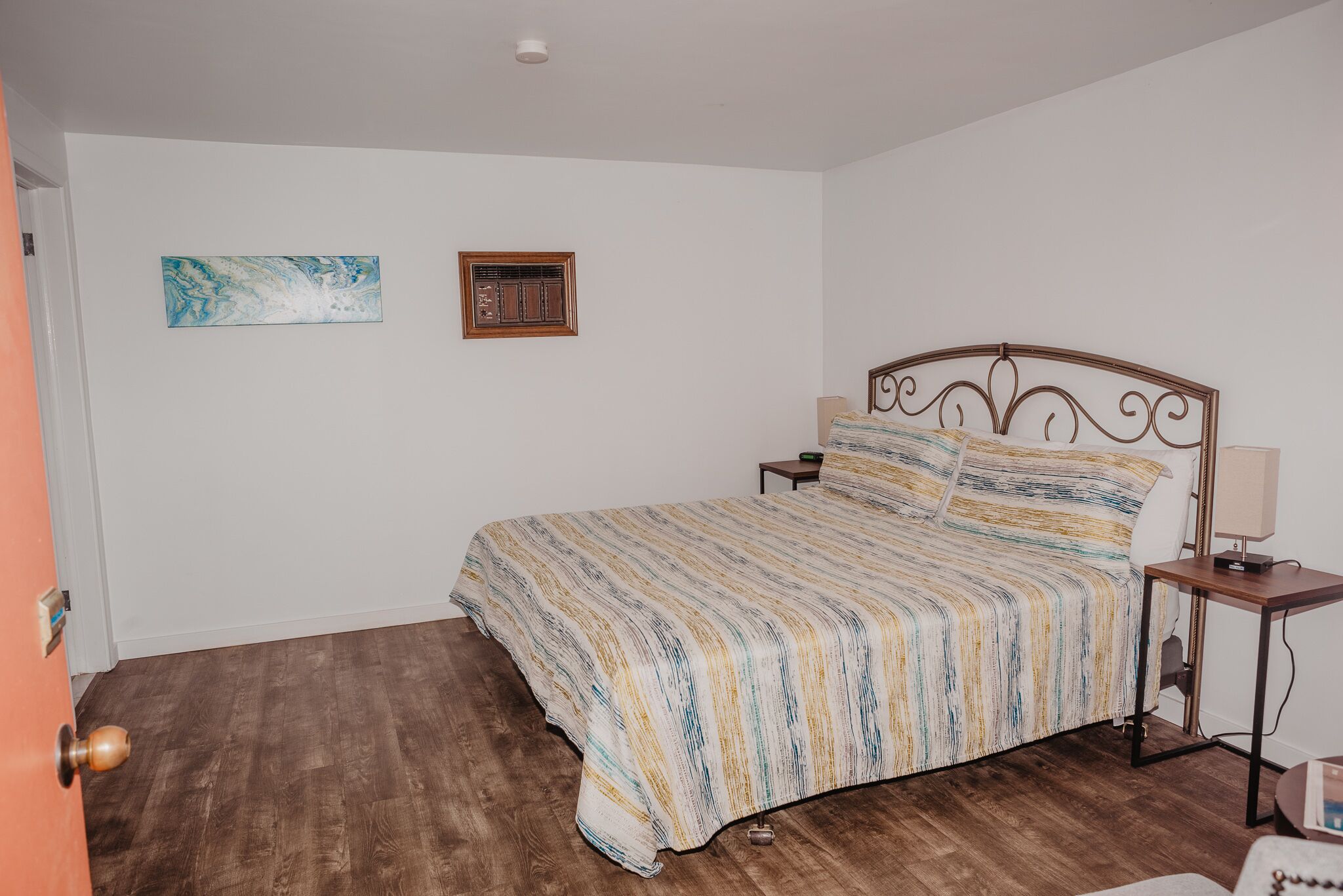 Un dormitorio con cama, mesita de noche, estante en la pared y una puerta.