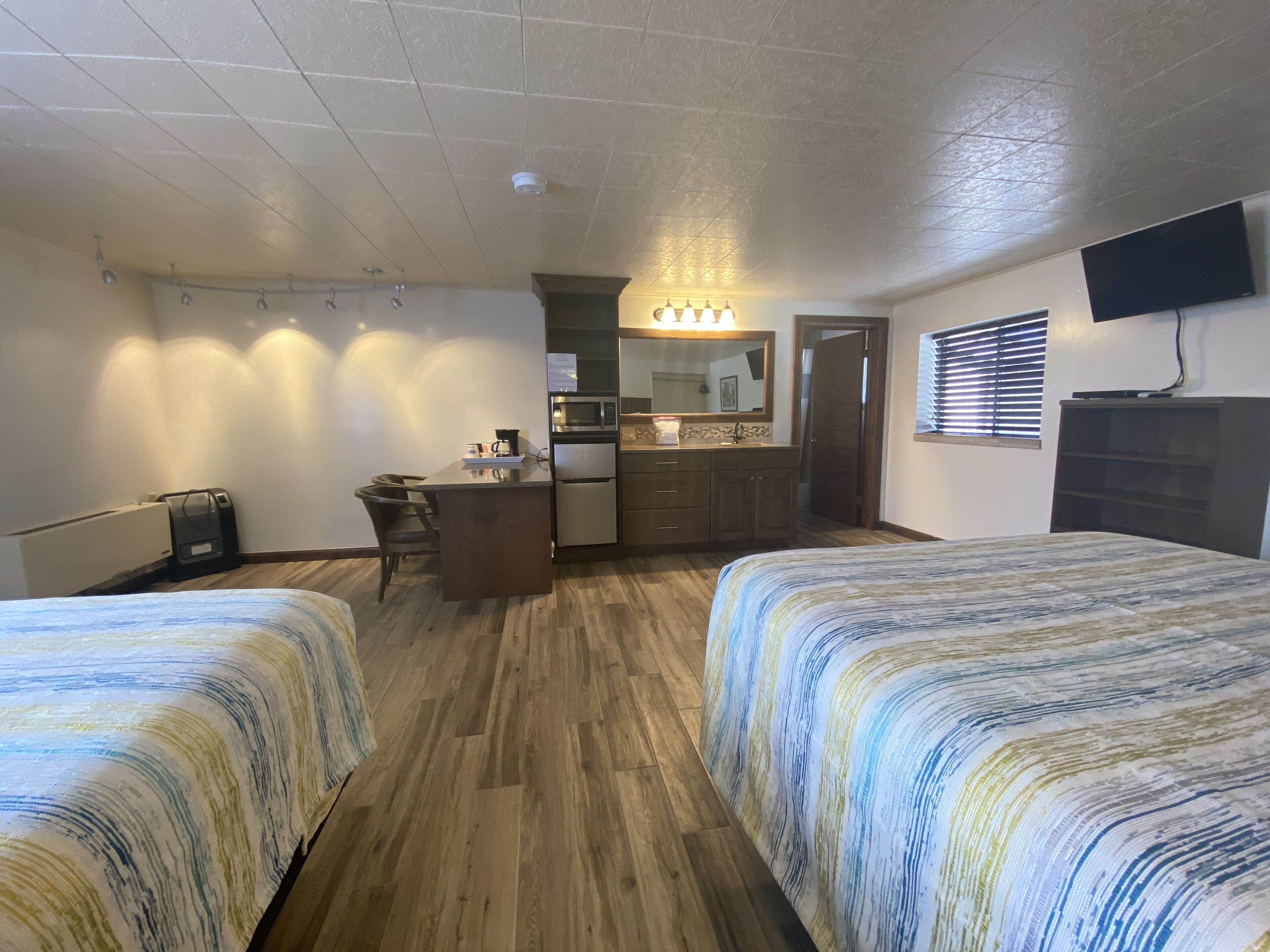 A hotel room with two beds, a kitchenette, a desk, and a TV.