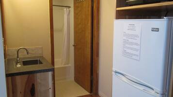 A compact kitchen with a built-in microwave, a refrigerator, and a wooden cabinet.
