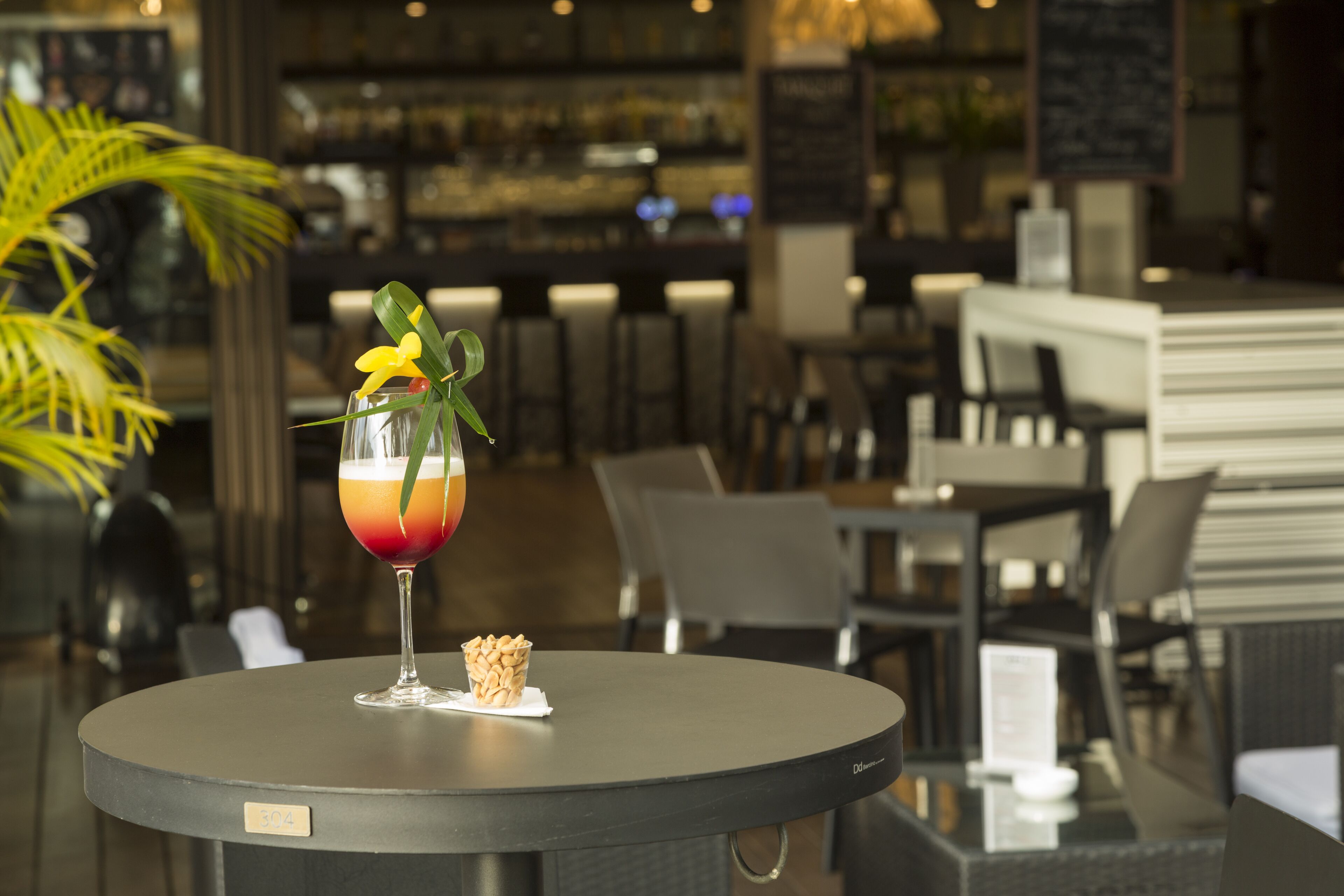 A bar area with a round table, a glass of drink with a garnish, and a small cupcake.