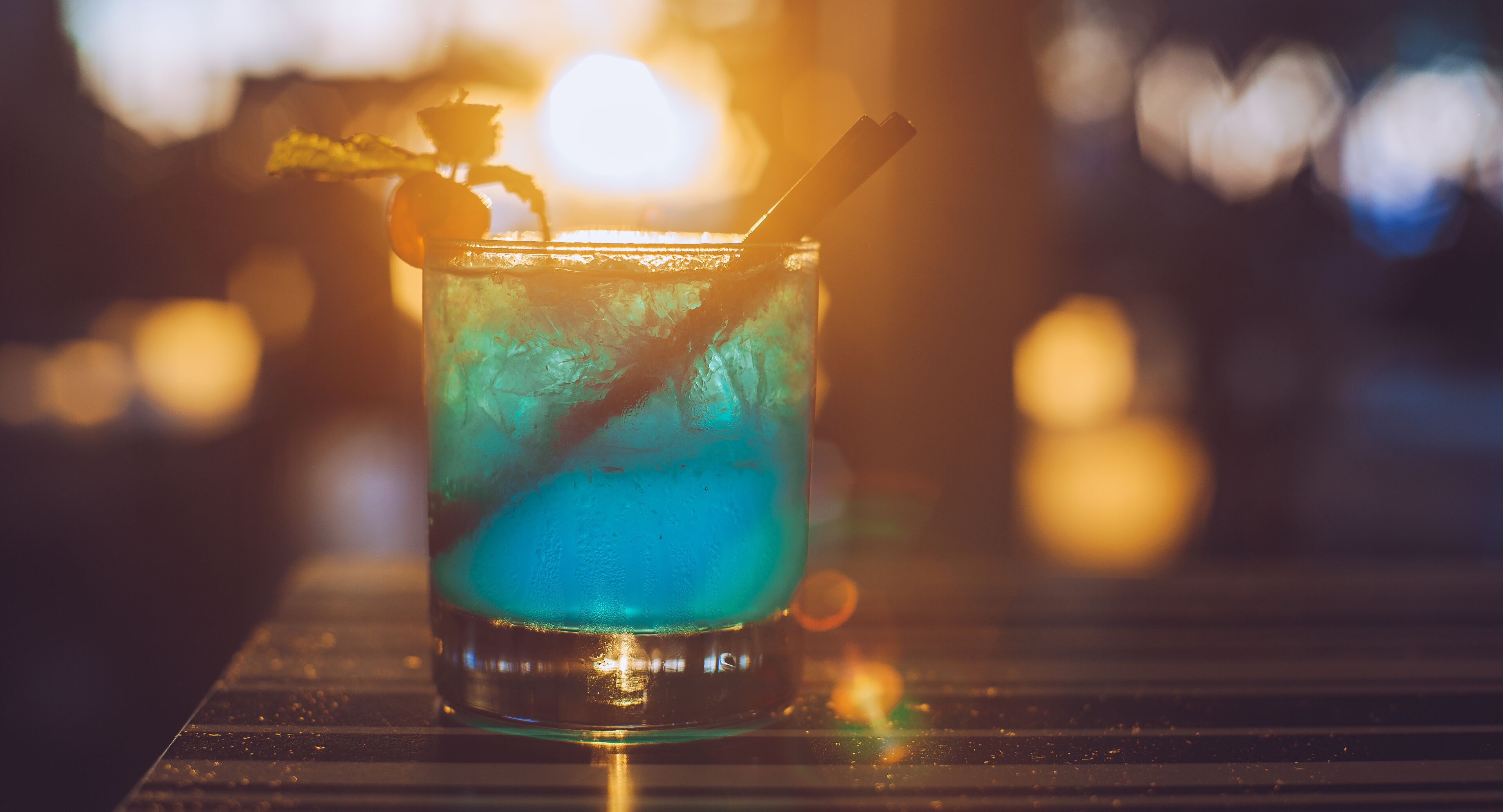 A glass with a blue drink, a straw, and a garnish on a bar counter.