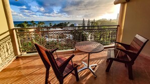 A balcony with two chairs and a small table, offering a view of the sea and palm trees.