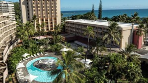 A resort with a pool surrounded by palm trees, a view of the ocean, and multiple buildings.