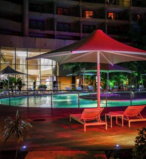 A pool area with lounge chairs and umbrellas, surrounded by a building with multiple floors and windows. - Nouvata (Nouméa)