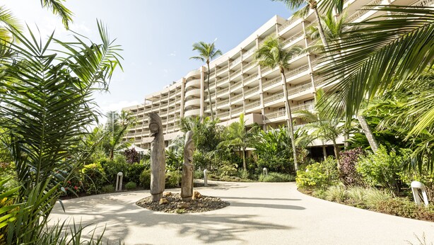 A hotel with multiple balconies, palm trees, and a central garden area.
