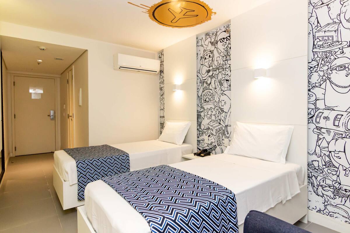 A hotel room with two beds, a wall mural, an air conditioning unit, and a door.