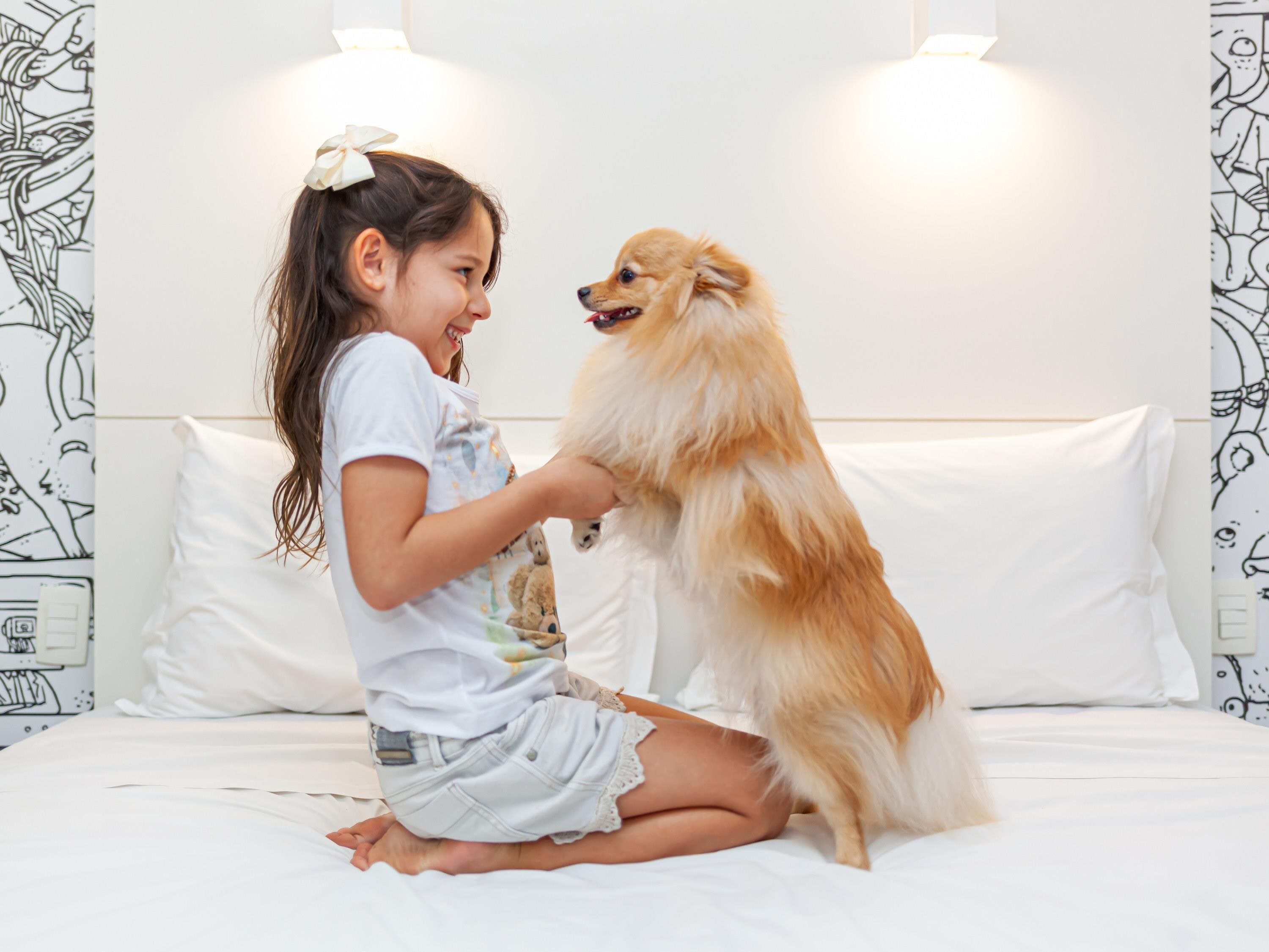 A child sitting on a bed with a dog.