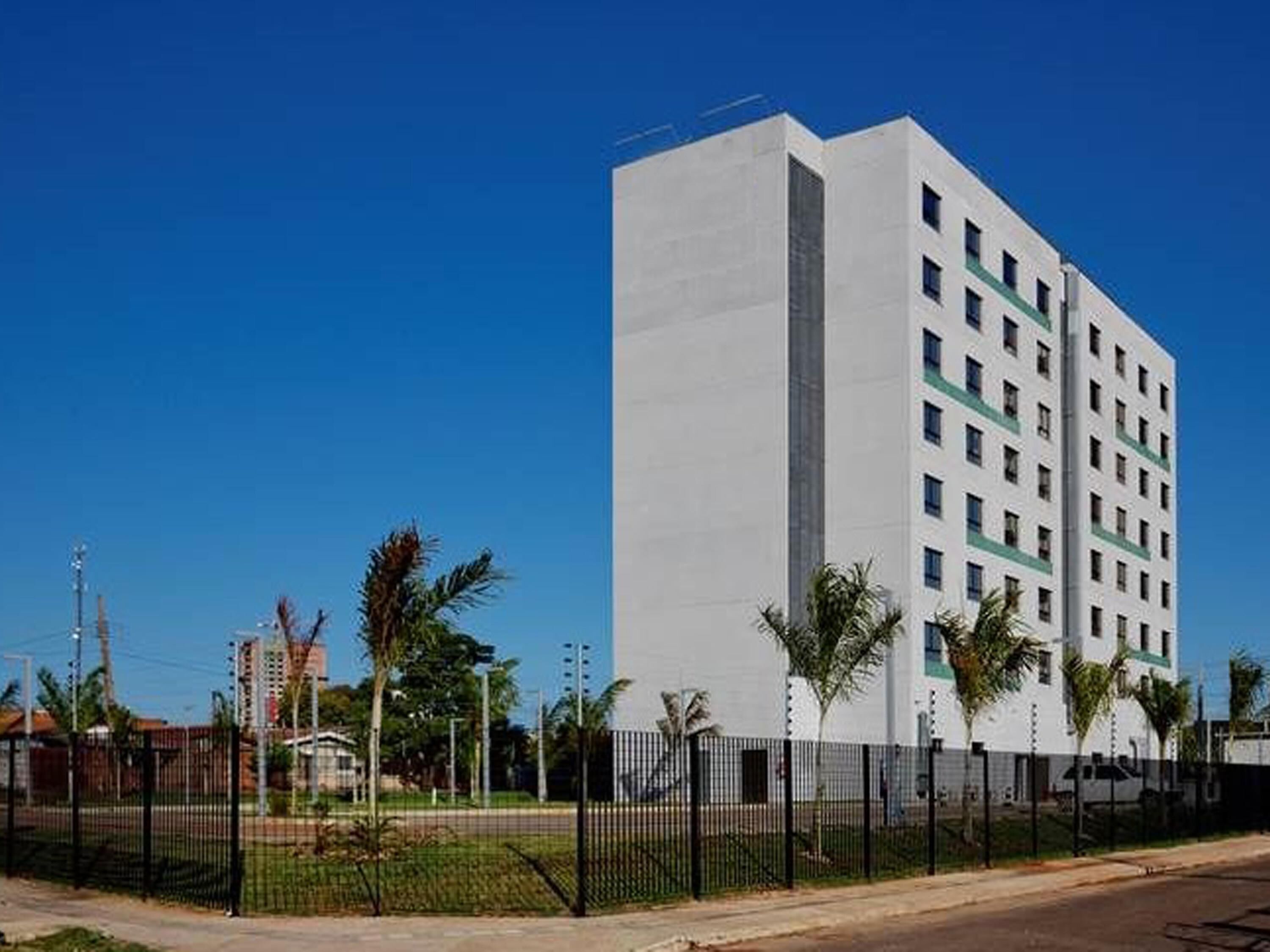 Un immeuble moderne à plusieurs étages, doté d’une façade plate, d’une série de fenêtres et d’une entrée fermée par un portail.
