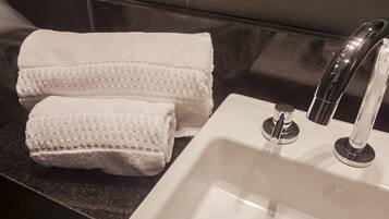 A bathroom with a white sink, two white towels, and a black countertop.