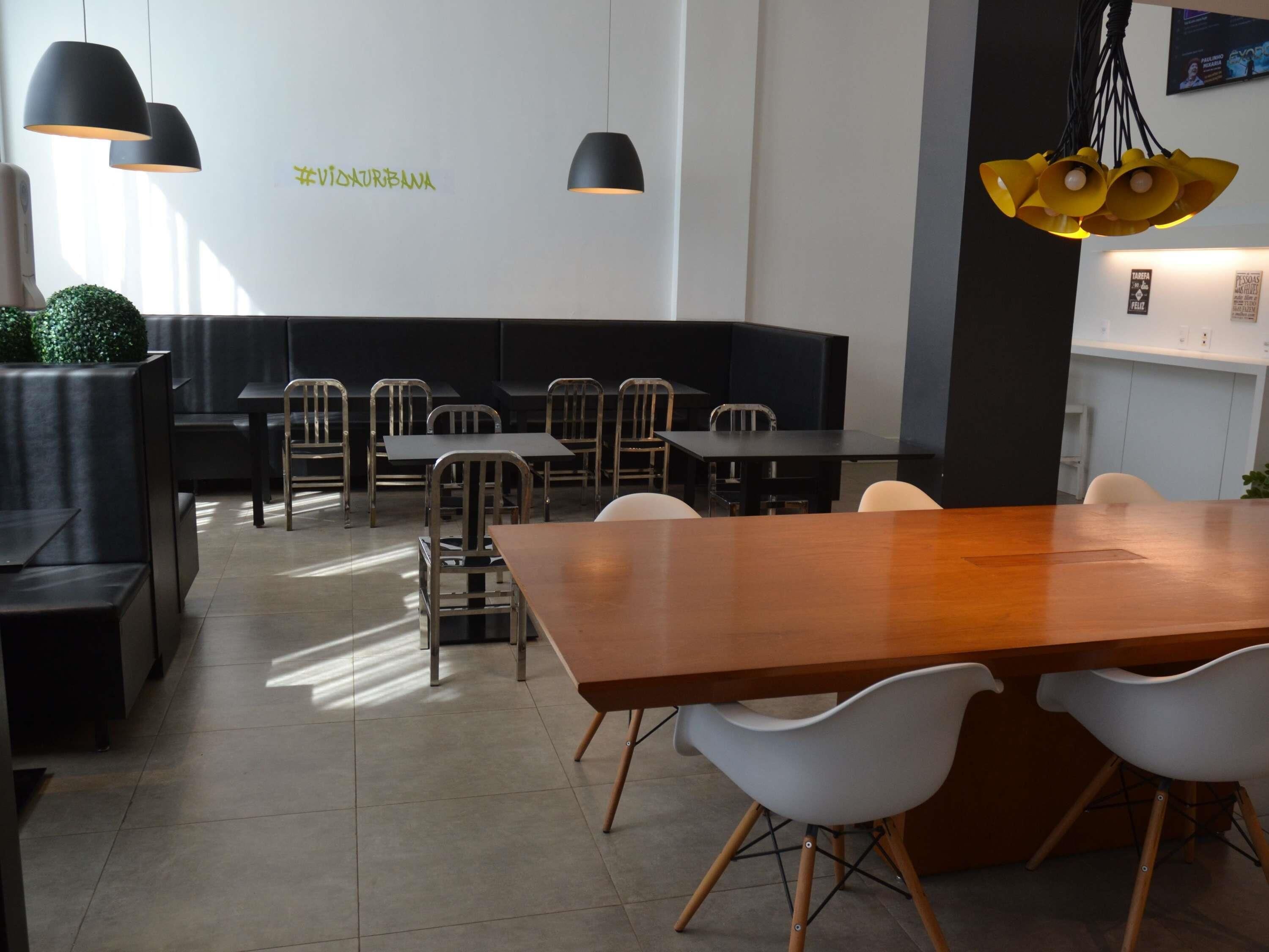 A modern restaurant interior with black and white furniture, pendant lighting, and a green wall sign.