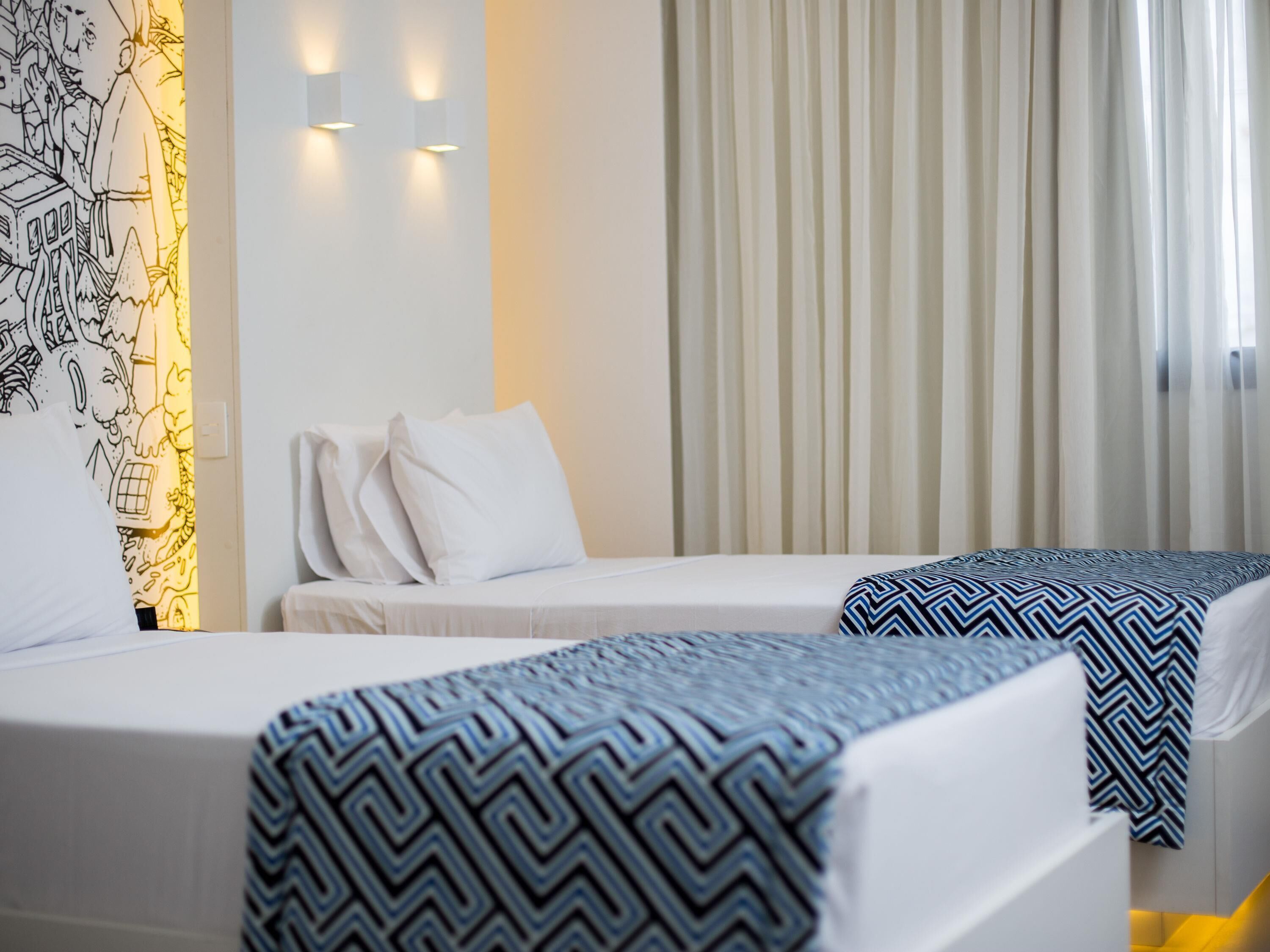 Habitación de hotel con dos camas, una lámpara de pared y una ventana con cortinas.