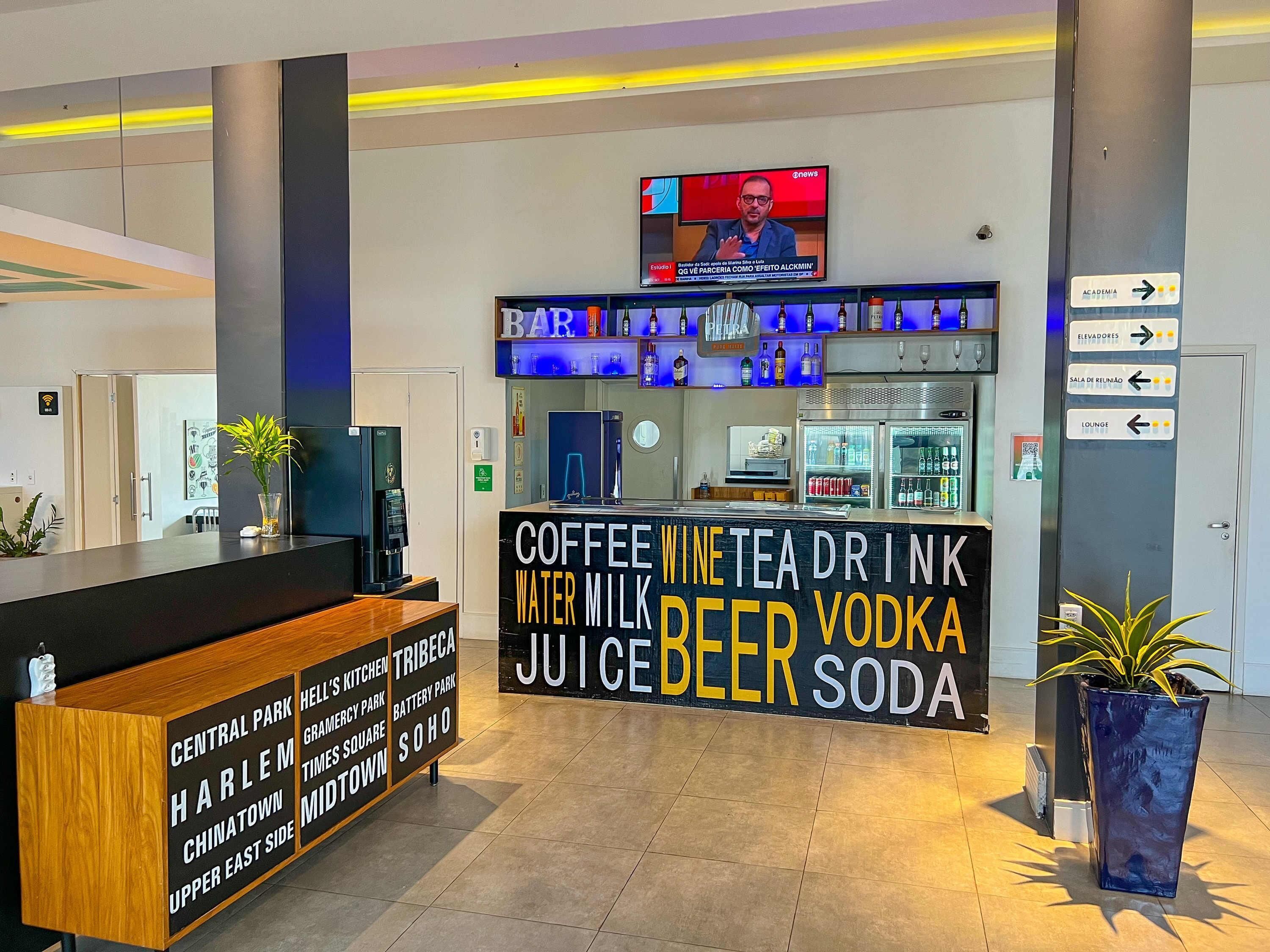Una zona de bar con un cartel que enumera bebidas y una pantalla de televisión encima.