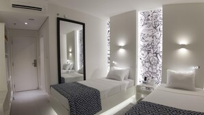A modern hotel room with a large bed, a smaller bed, a mirror, and a wall with a black and white pattern.