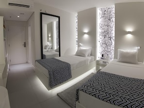 Una habitación de hotel moderna con una cama grande, una cama más pequeña, un espejo y una pared con diseño en blanco y negro.