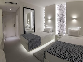 Una habitación de hotel moderna con una cama grande, una cama más pequeña, un espejo y una pared con diseño en blanco y negro.