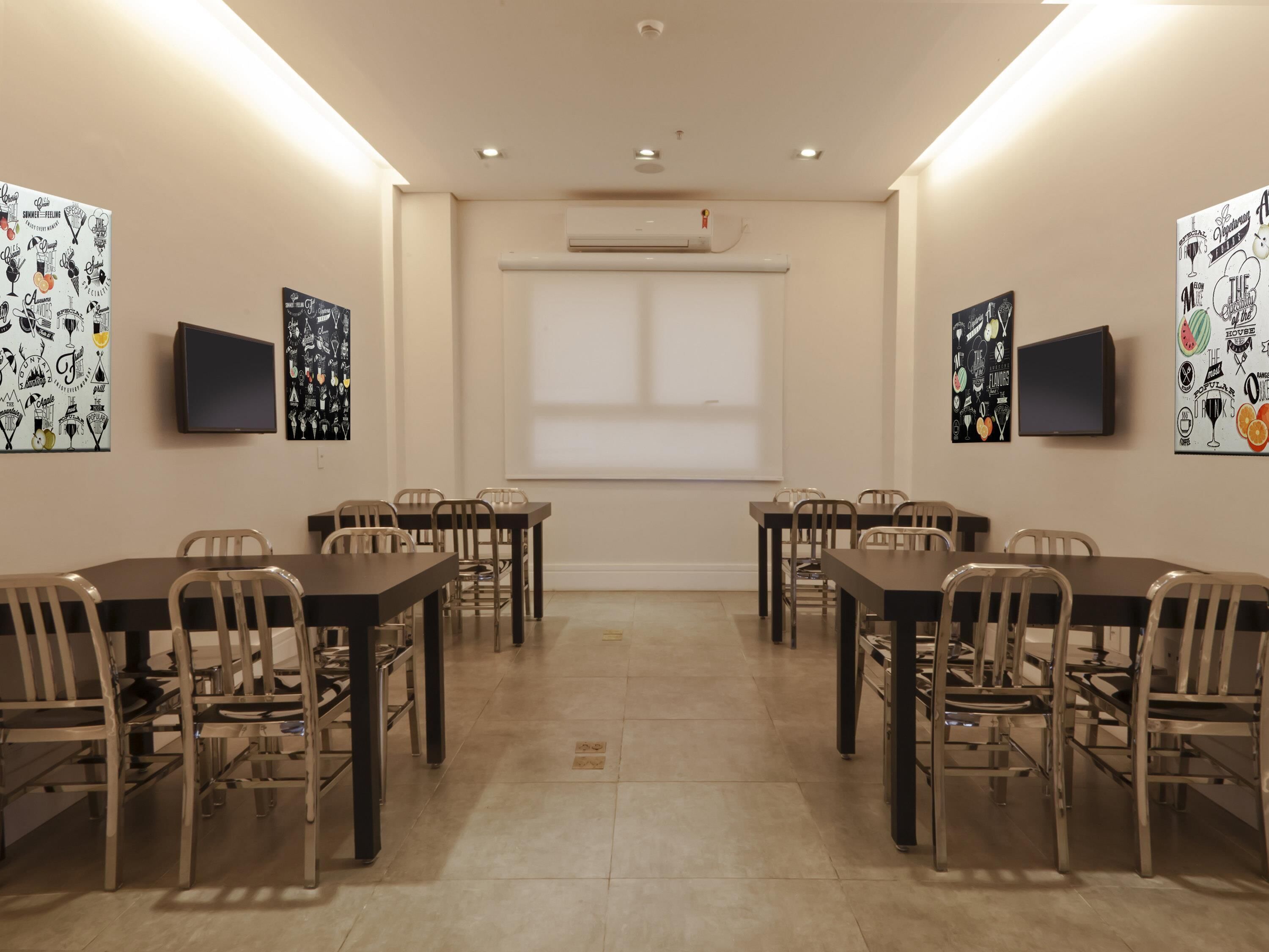 A conference room with a long table, chairs, a projector screen, and wall art.