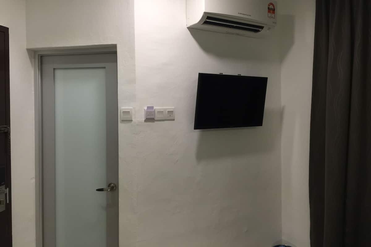 A room with a white door, a mounted air conditioner, a flat-screen TV, and a wall socket.