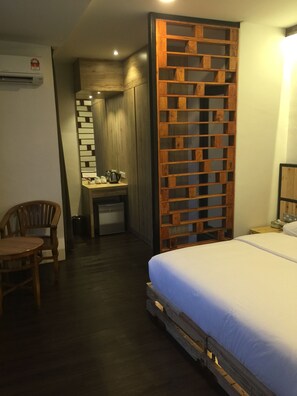 A hotel room with a bed, a wooden partition, a desk with a chair, and a small table with a lamp. - The Oikos Hotel (Pontian)