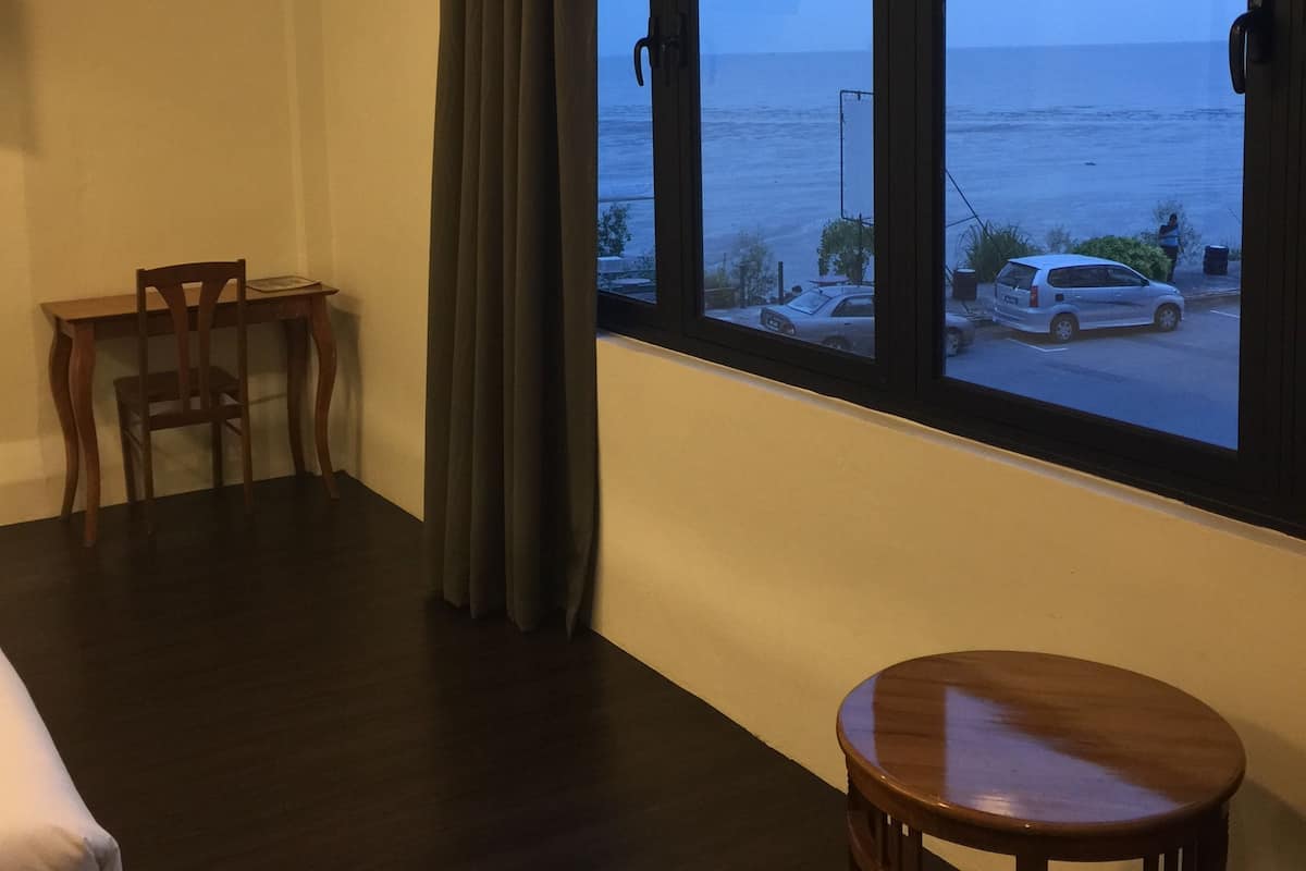A room with a large window overlooking the sea, a wooden desk, a chair, and a small round table.