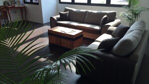 A modern living room with a sofa, a coffee table, and a desk with a computer. - The Oikos Hotel (Pontian)