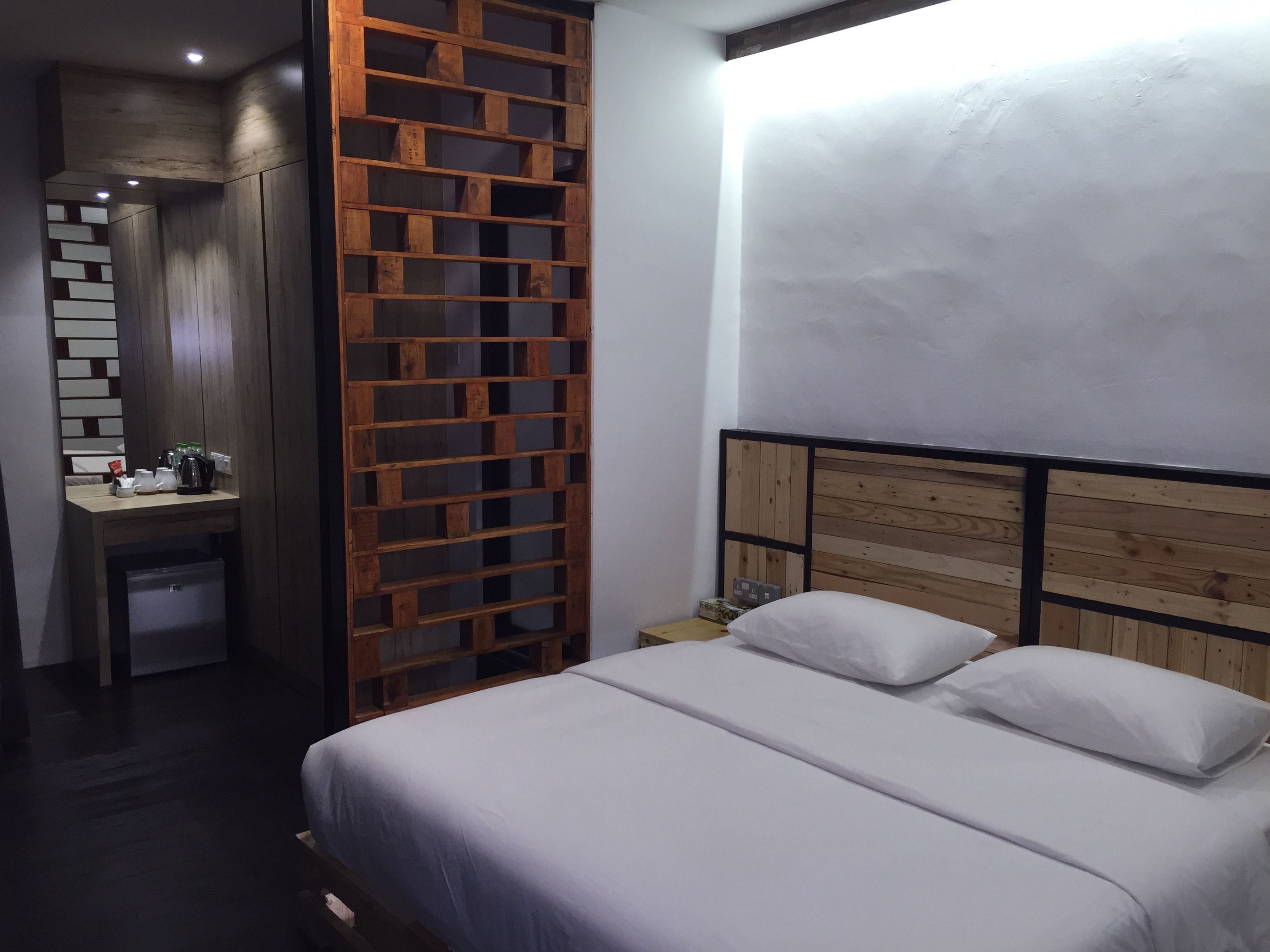 A bedroom with a bed, a wooden headboard, a desk with a chair, and a small cabinet.