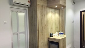 A hotel room with a wooden wardrobe, a small fridge, a water dispenser, and a coffee maker on the counter. - The Oikos Hotel (Pontian)