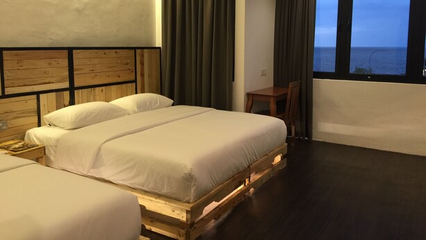 A hotel room with two beds on wooden pallets, a small table, and a view of the sea through large windows. - The Oikos Hotel (Pontian)