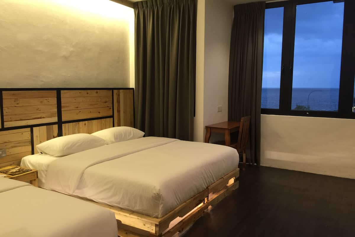 A hotel room with two beds on wooden pallets, a small table, and a view of the sea through large windows.
