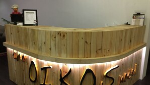 A wooden reception desk with illuminated letters spelling "OIKOS Suites." - The Oikos Hotel (Pontian)