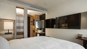 A hotel room with a large bed, a bedside table, a mirror, a window with blinds, and a wall-mounted TV.