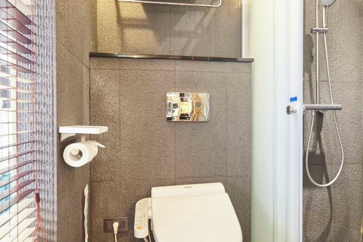A bathroom with a toilet, a towel, a shower, and a toilet paper holder.