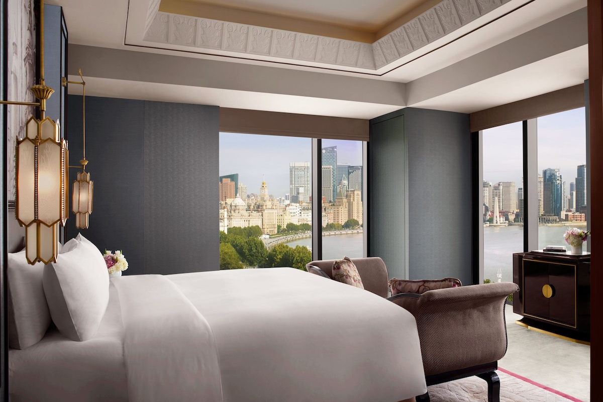 A modern hotel room with a large bed, a seating area, and a view of the city.