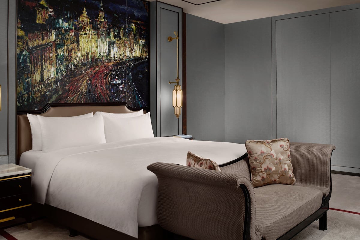 A hotel room with a large bed, a nightstand, a sofa with a cushion, and a wall-mounted lamp.