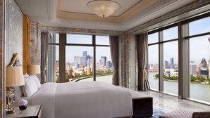 A spacious hotel room with a large bed, a sitting area, and a view of a cityscape through large windows. - The St. Regis on the Bund, Shanghai (Shanghai)