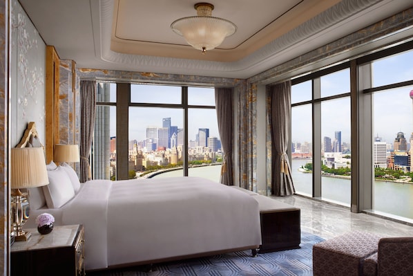 Ein geräumiges Hotelzimmer mit einem großen Bett, einer Sitzecke und Blick auf eine Stadtlandschaft durch große Fenster.