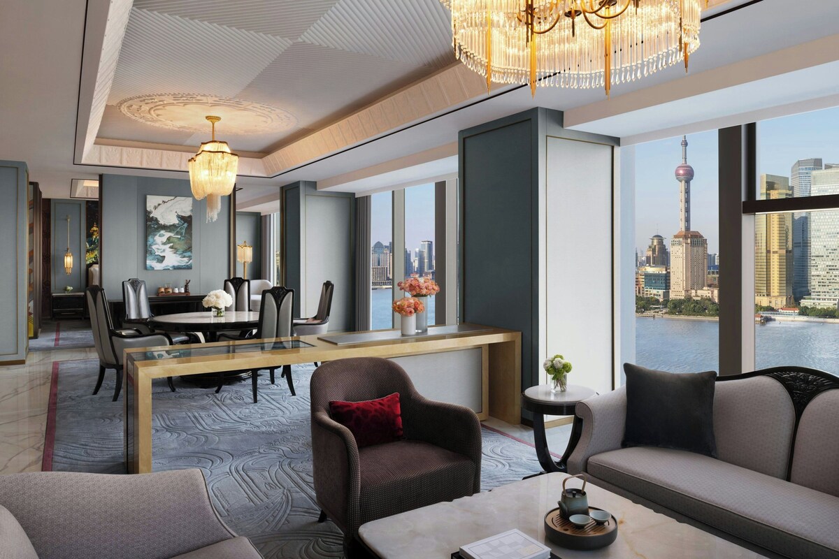 Habitación de hotel moderna con comedor, sofá y vistas a un paisaje urbano.