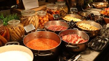 En buffet med forskellige retter i metalbeholdere, blandt andet bønner, kød og grøntsager.