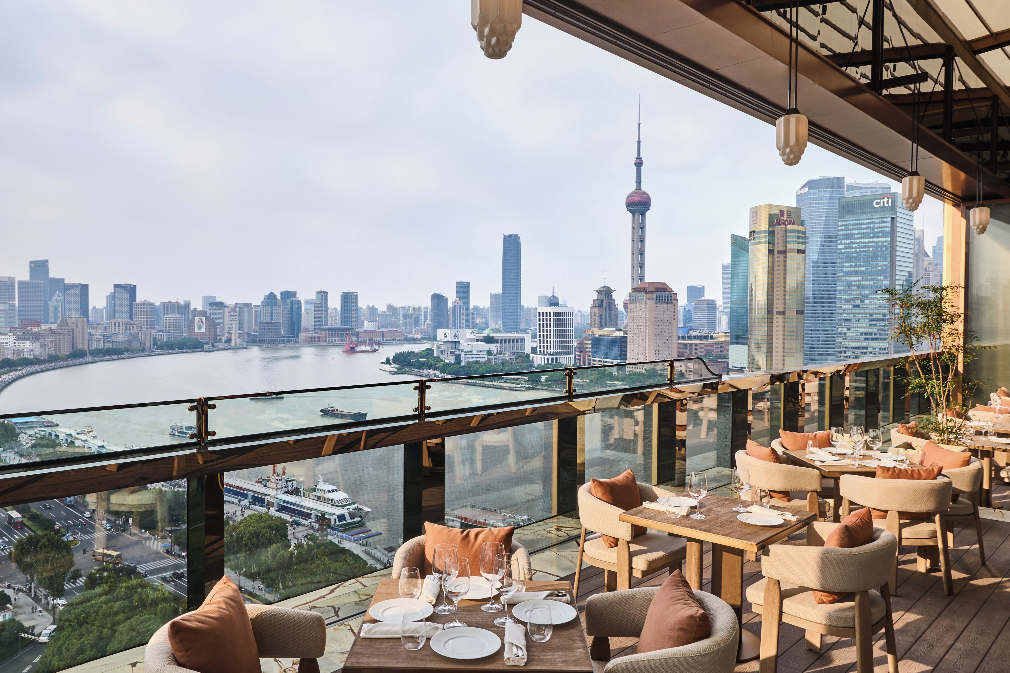 A restaurant with tables set for dining, overlooking a city skyline and river.