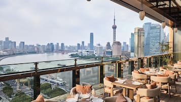 A restaurant with tables set for dining, overlooking a city skyline and river.