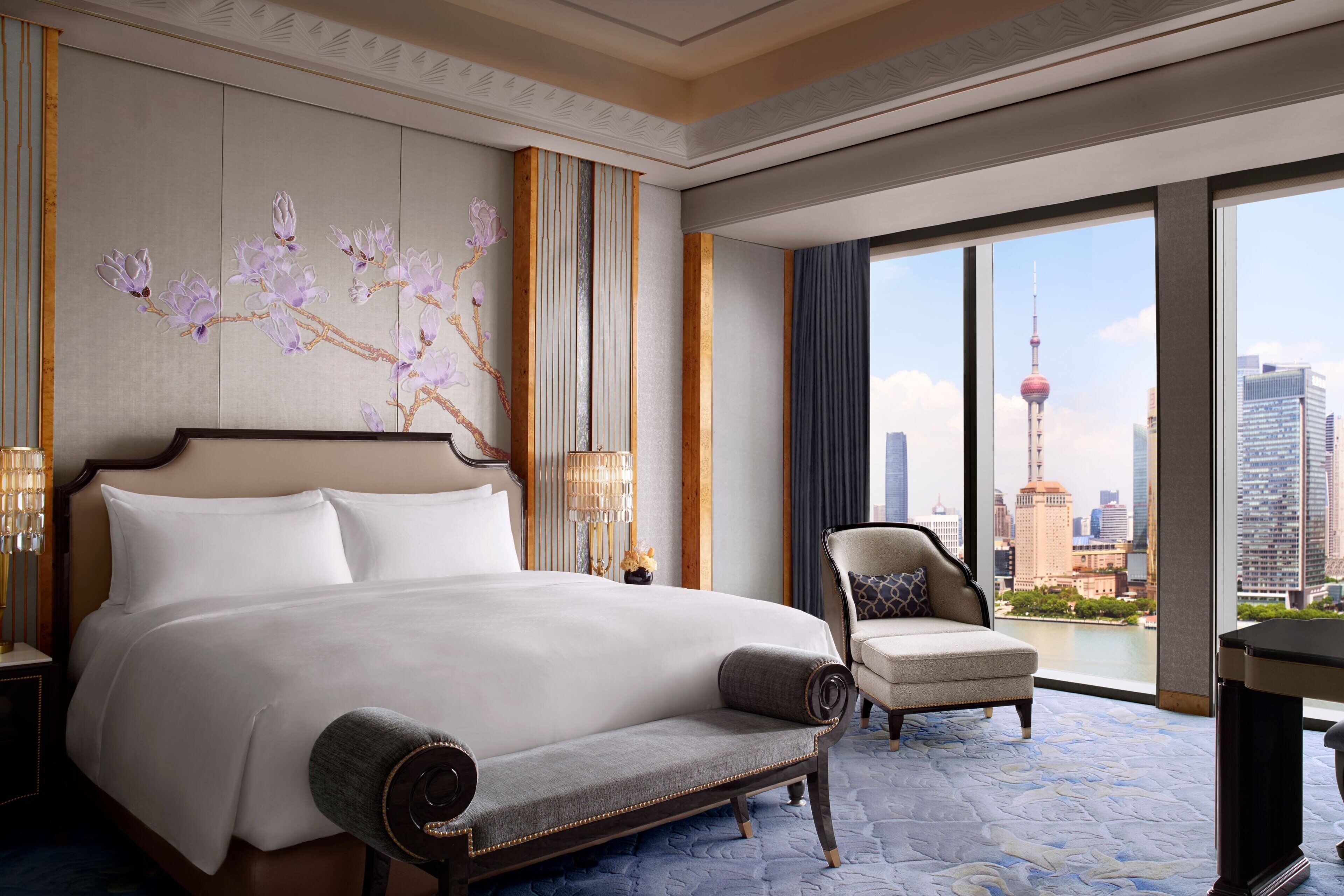 A hotel room with a large bed, a chair, and a view of a cityscape including a tower.