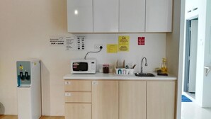 Cocina compacta con microondas, pileta y alacenas. Hay carteles en la pared y un dispensador de agua.