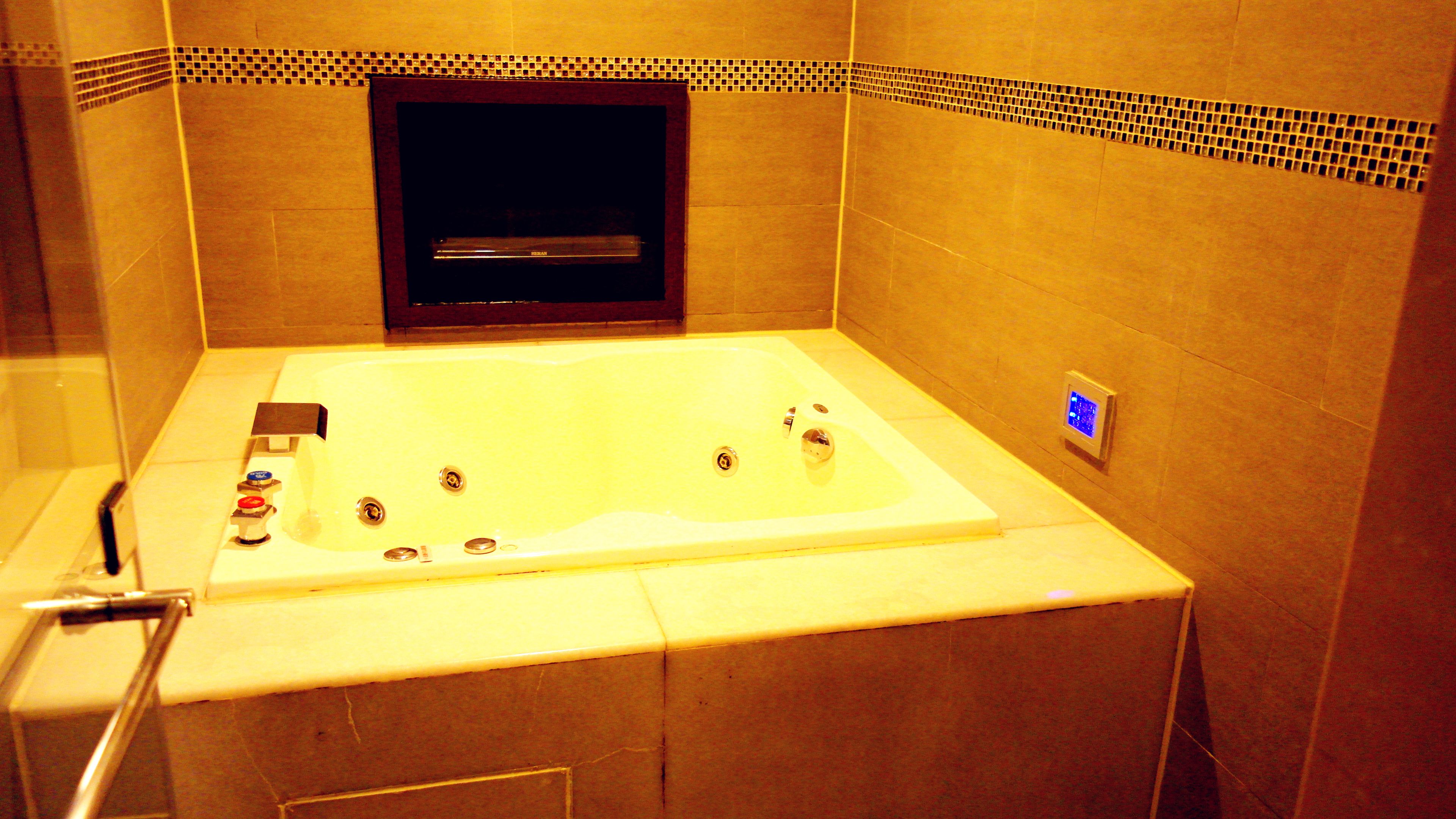 A large bathtub with multiple faucets, a control panel, and a tiled wall with a decorative border.