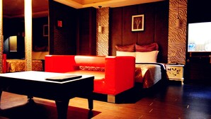 A hotel room with a red sofa, a bed with white bedding, a nightstand with a lamp, and a wall with a textured pattern.