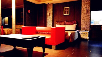 A hotel room with a red sofa, a bed with white bedding, a nightstand with a lamp, and a wall with a textured pattern.