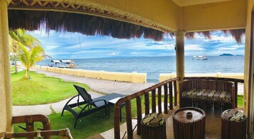 Un área de estar al aire libre techada con vista al mar, una palmera y un barco a lo lejos.