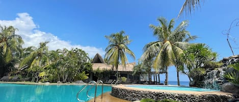 A clear blue pool with a stone border, surrounded by palm trees and lounge chairs.
