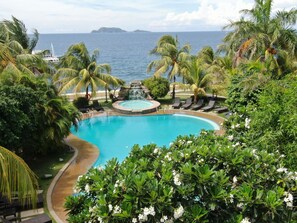 A pool surrounded by palm trees and a view of the ocean. - Thalatta Resort (Zamboanguita)